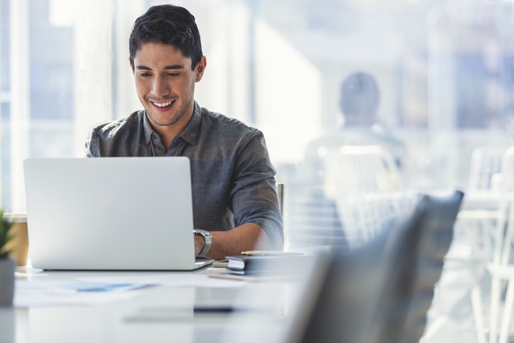 Businessman smiling and working on a laptop in a modern office, with staffing agency solutions from Fort Lee supporting his career growth.