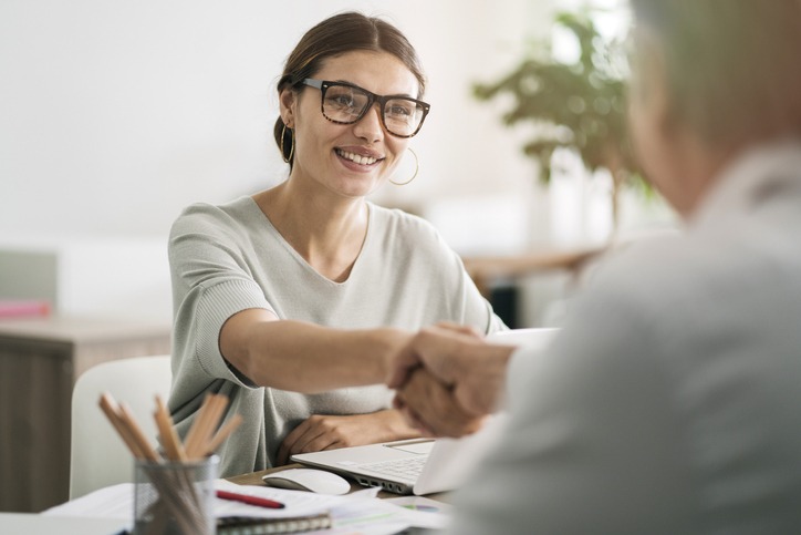 Woman wearing dark-rimmed glasses shaking hands with a candidate at a staffing agency for top talent.
